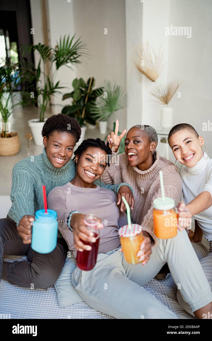 Lächelnde multiethnische Freundinnen mit Saft im Wohnzimmer Stockfoto