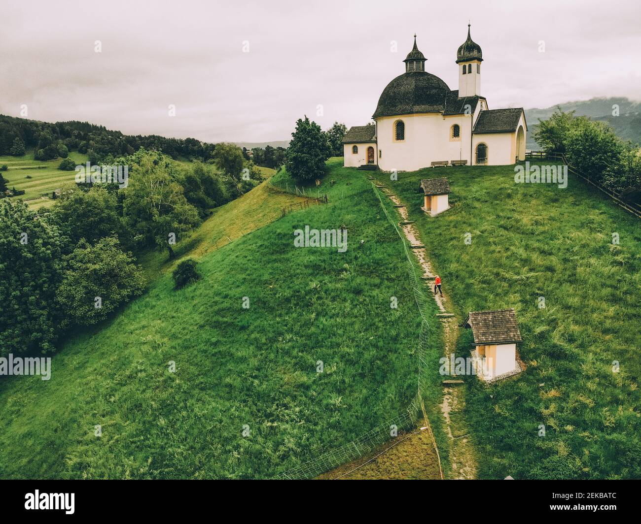 Luftaufnahme einer Frau, die auf einem grünen Hügel in Richtung Kapelle geht Stockfoto