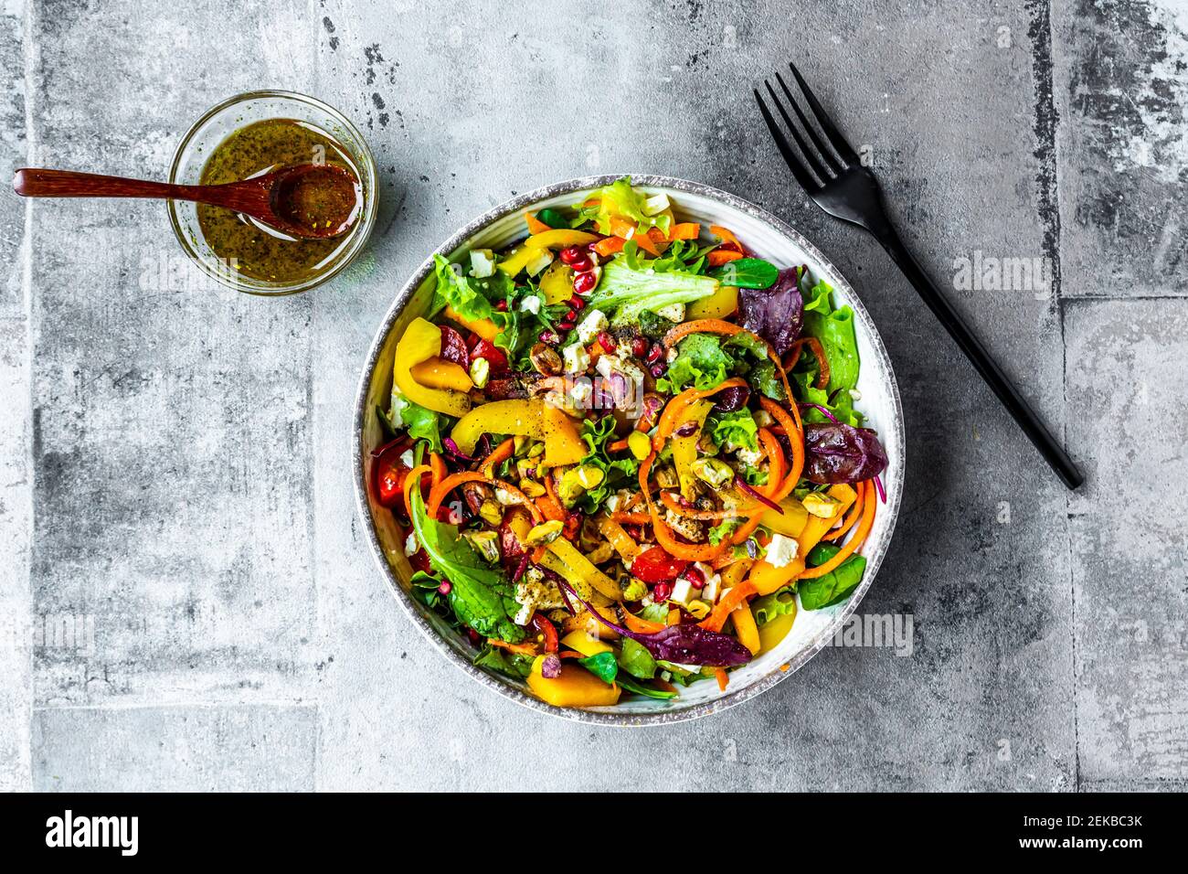 Gemischter Salat mit Paprika, Feta, Pistazien, Tomaten, Granatapfelkernen, Kaki und Dressing Stockfoto