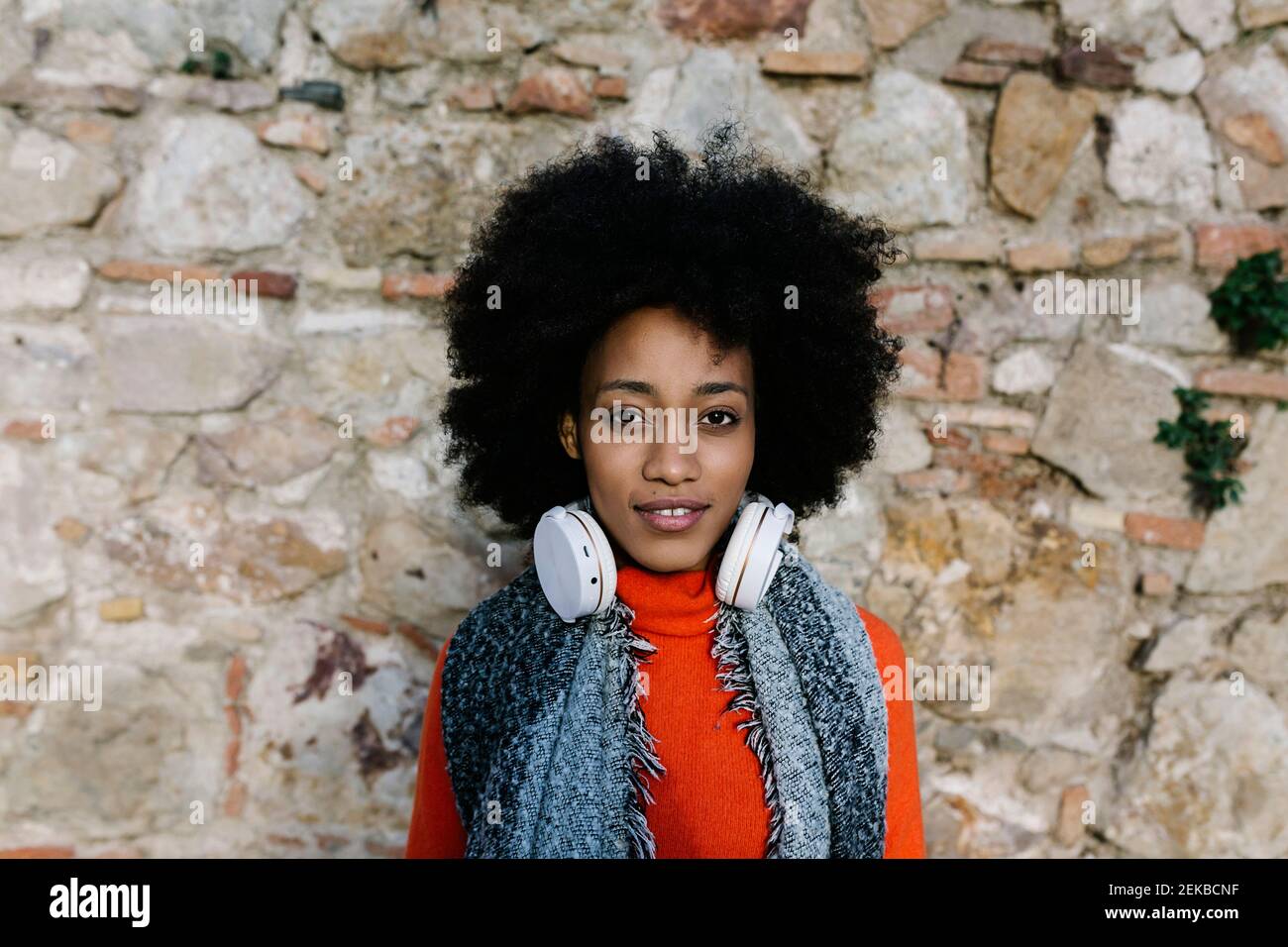 Junge Frau mit Kopfhörern in warmer Kleidung an der Steinwand Stockfoto