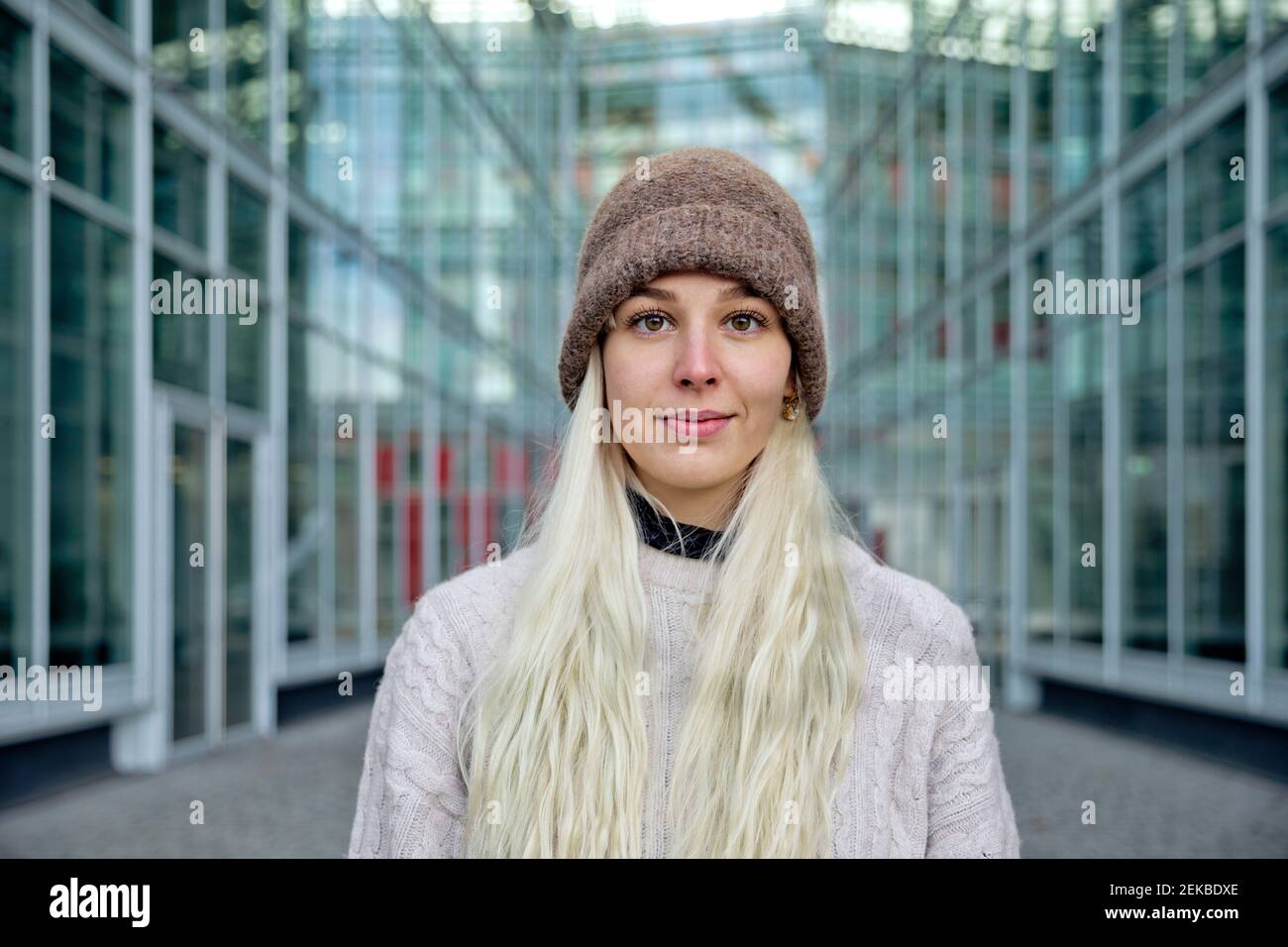 Junge Frau in warmer Kleidung, die gegen ein modernes Gebäude steht Stadt Stockfoto