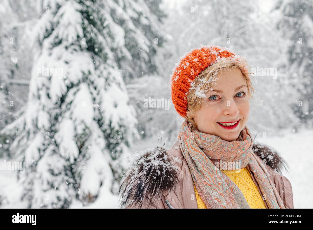 Reife Frau lächelt, während sie im Winter im Wald steht Stockfoto