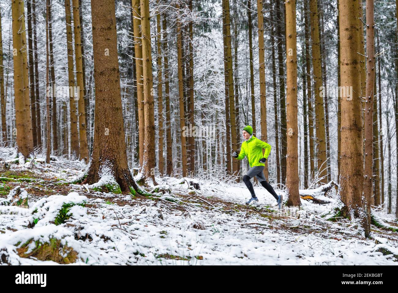 Junger männlicher Sportler joggt bei verschneitem Wetter im Wald Stockfoto