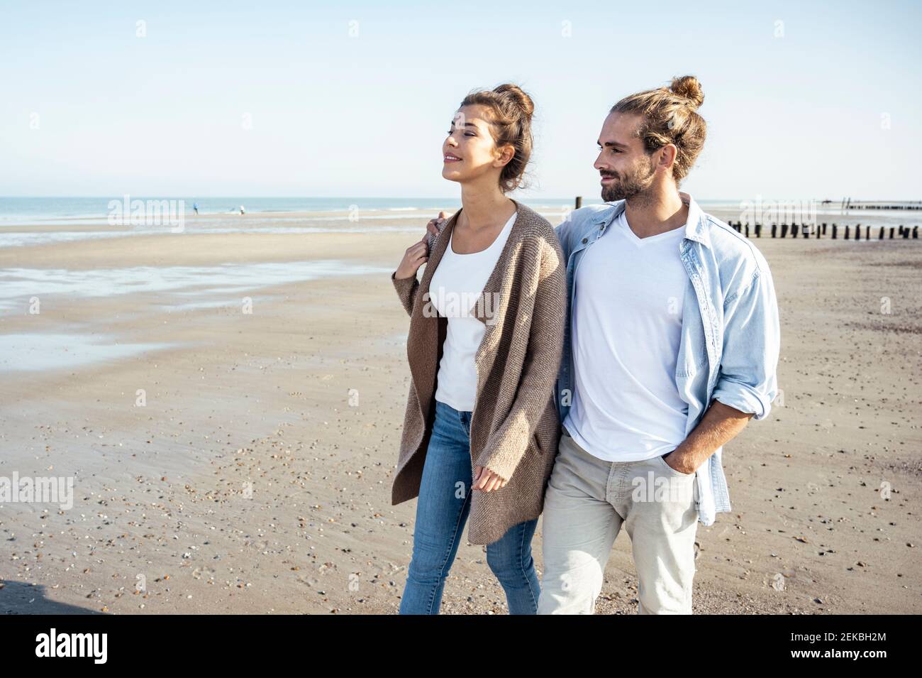 Lächelnde Freundin und Freund schauen weg, während sie am Strand spazieren gehen Am Wochenende Stockfoto