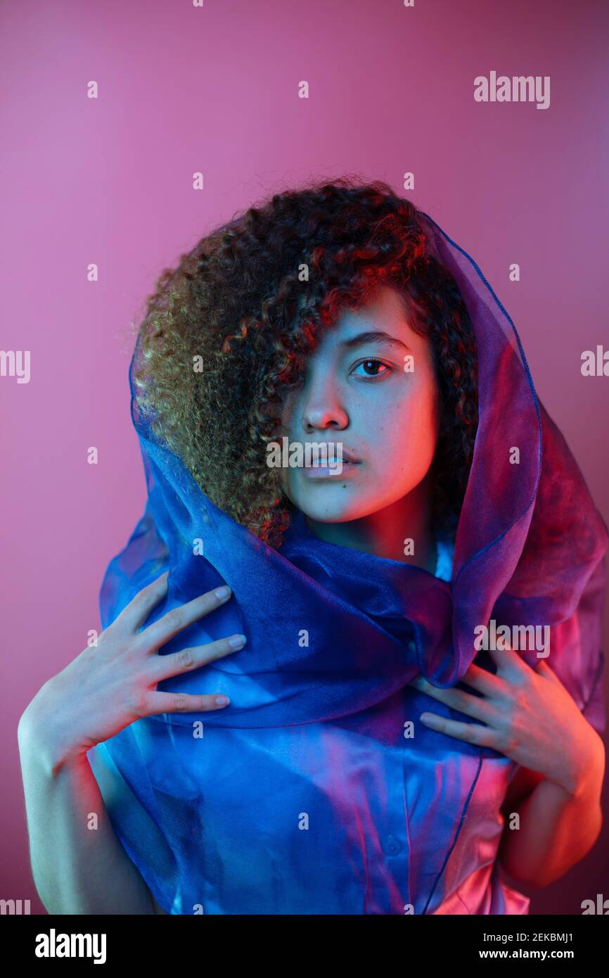 Schöne Frau mit lockigen Haaren trägt Schal vor lila Hintergrund Stockfoto