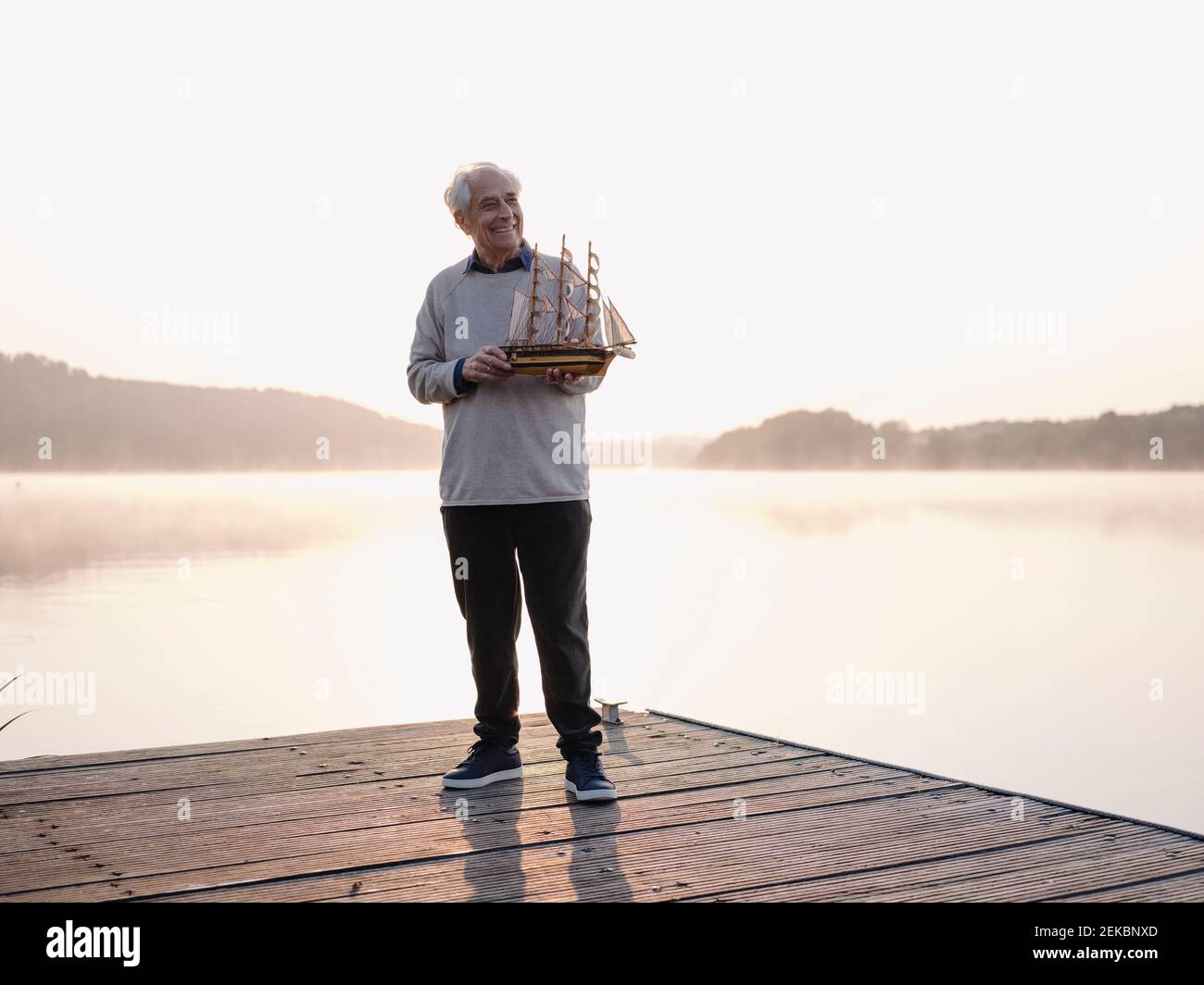 Lächelnder älterer Mann, der das Segelschiff hält, während er auf dem Pier steht Stockfoto