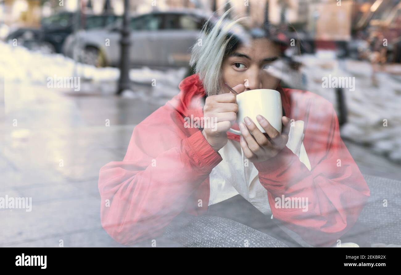 Asiatischer Mann trinkt Kaffee durch Glas gesehen im Café während Winter Stockfoto