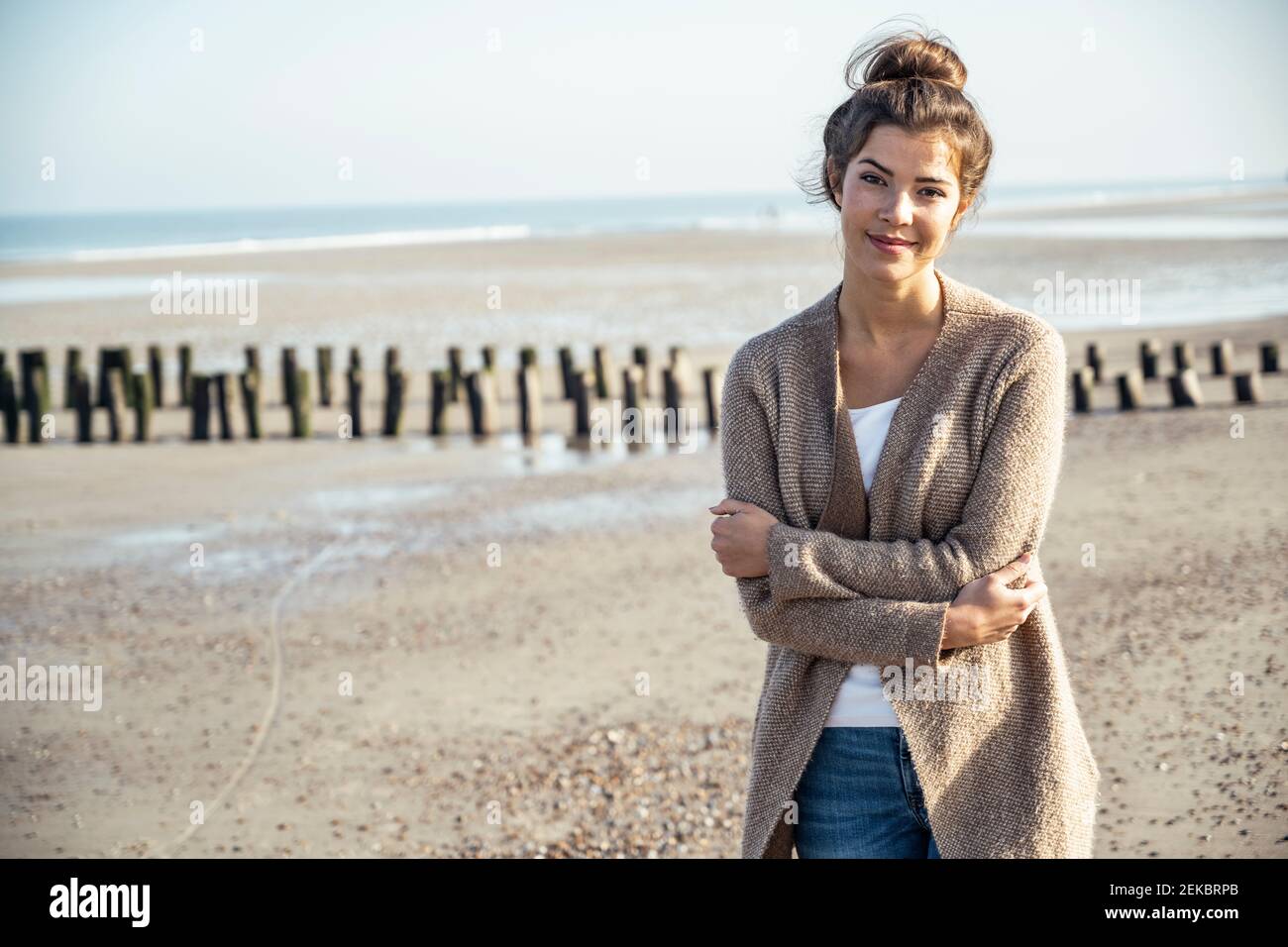 Lächelnde Frau mit gekreuzten Armen am Strand Stockfoto