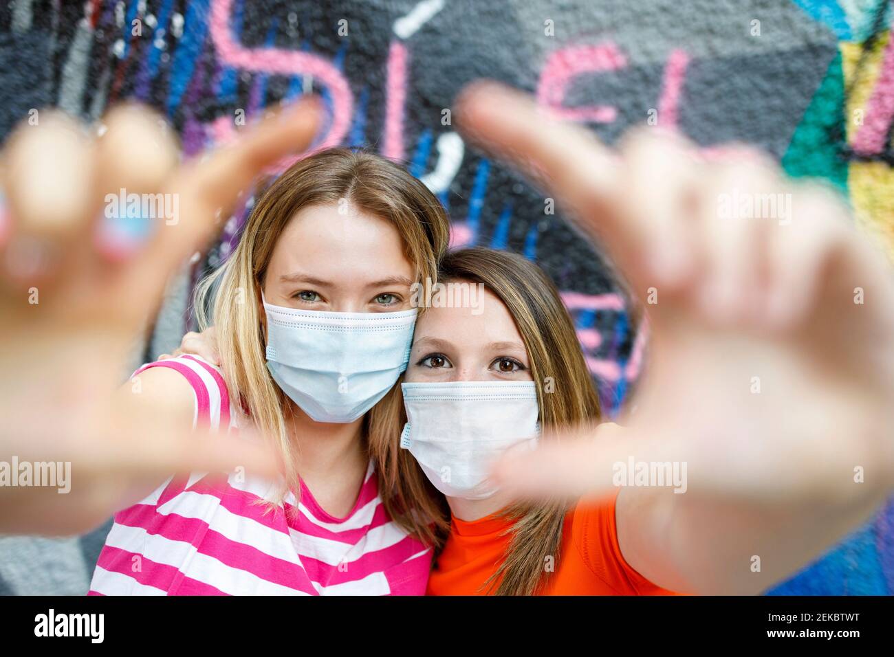 Weibliche Freundinnen tragen Schutzmasken und machen Selfie gegen mehrfarbige Wände Stockfoto