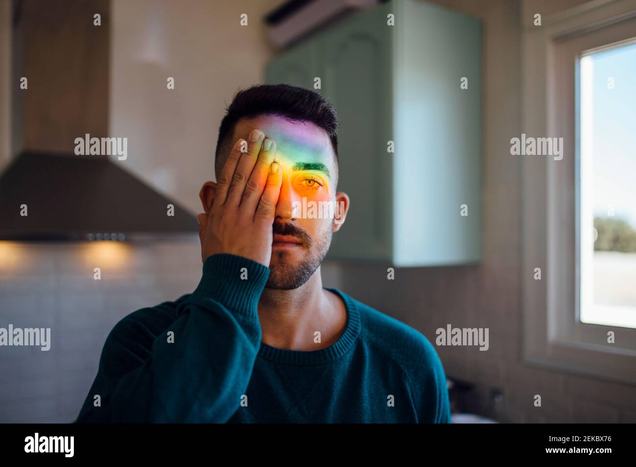 Regenbogenlicht trifft Gesicht des jungen Mannes, der ein Auge bedeckt Mit der Hand Stockfoto