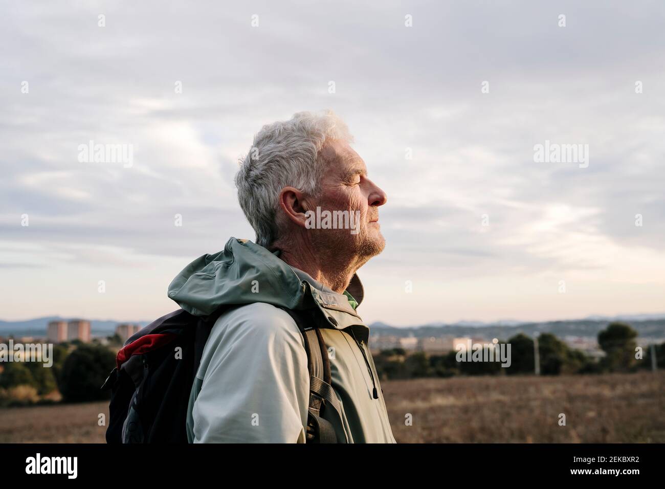 Älterer männlicher Wanderer mit geschlossenen Augen auf dem Land während des Sonnenuntergangs Stockfoto