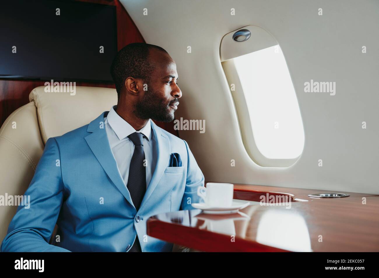 Junger Geschäftsmann, der durch das Fenster schaut, während er durch den Privatjet reist Stockfoto
