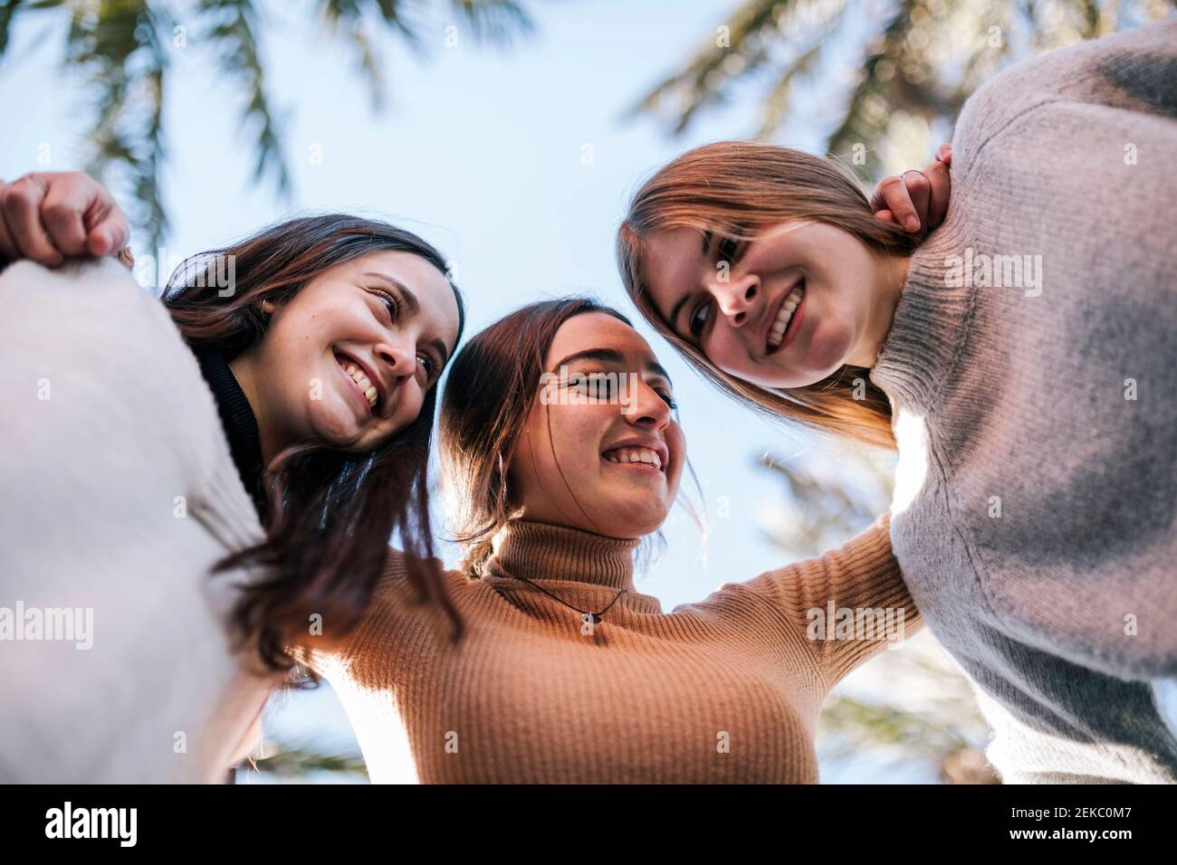 Lächelnde Freundinnen, die im Park gegen den klaren Himmel husten Stockfoto