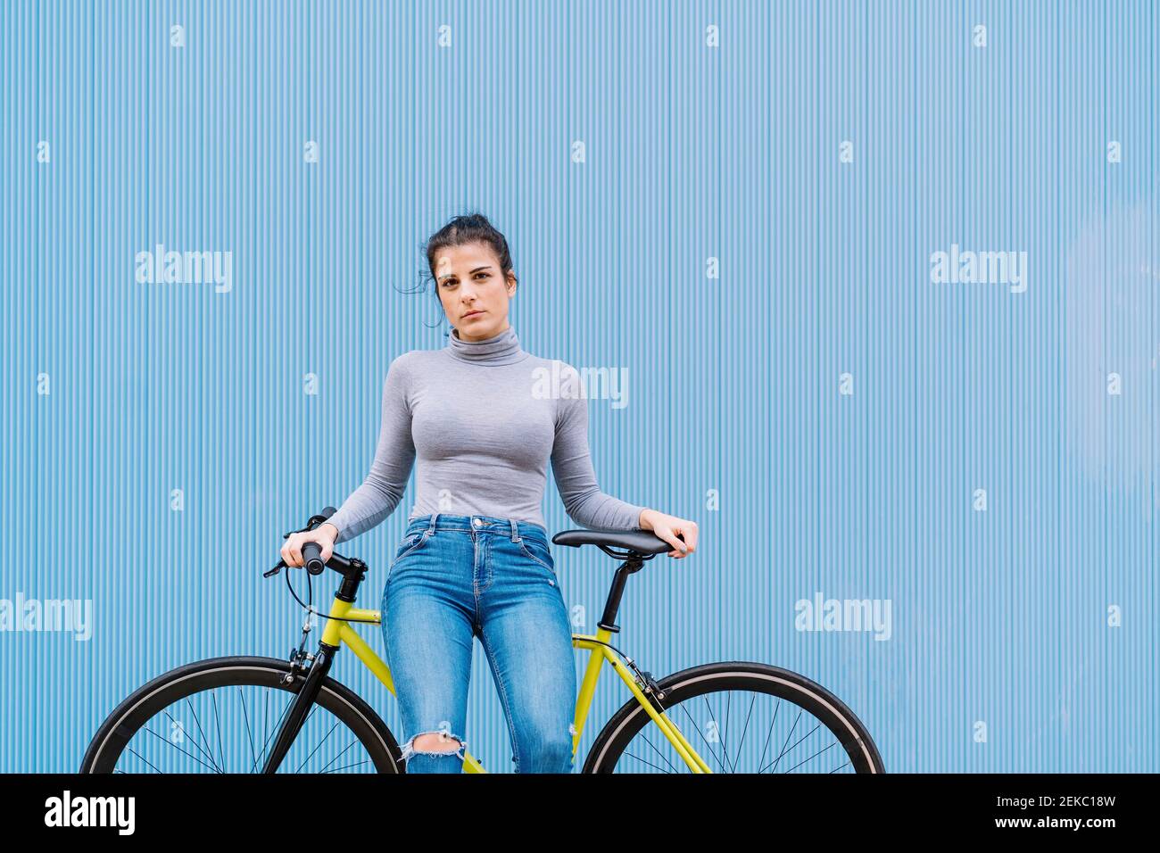 Selbstbewusste Frau mittleren Erwachsenen sitzt auf Fixie Fahrrad gegen blau Wand Stockfoto