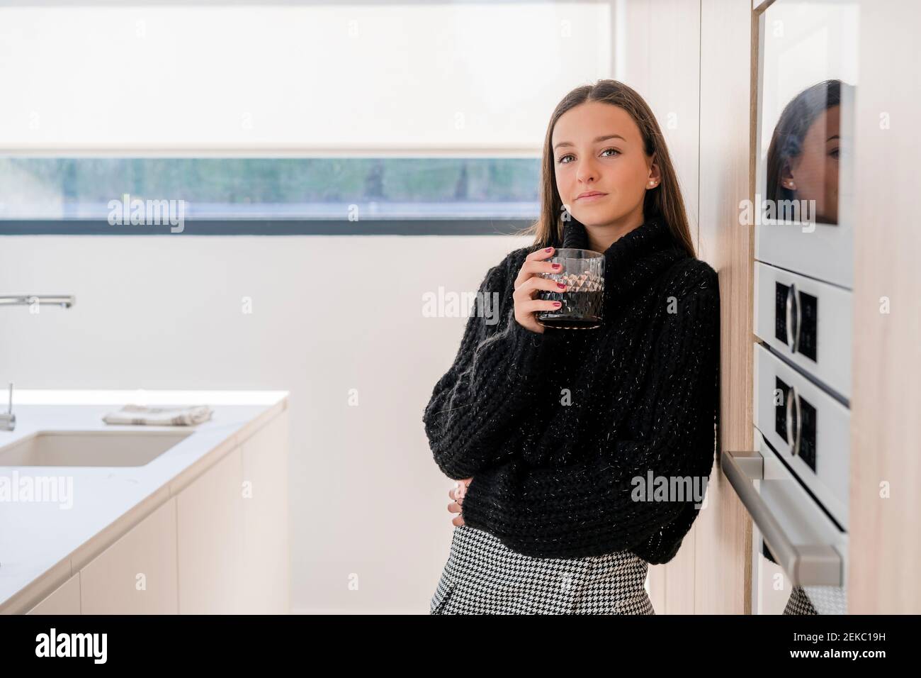 Teenager-Mädchen mit Getränk stehen bei Gerät in der Küche Stockfoto