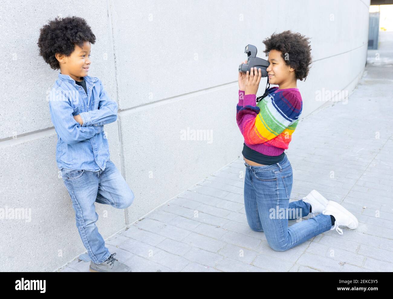 Schwester fotografiert Bruder durch die Kamera, während sie sich auf die Knie kniet Fußweg Stockfoto