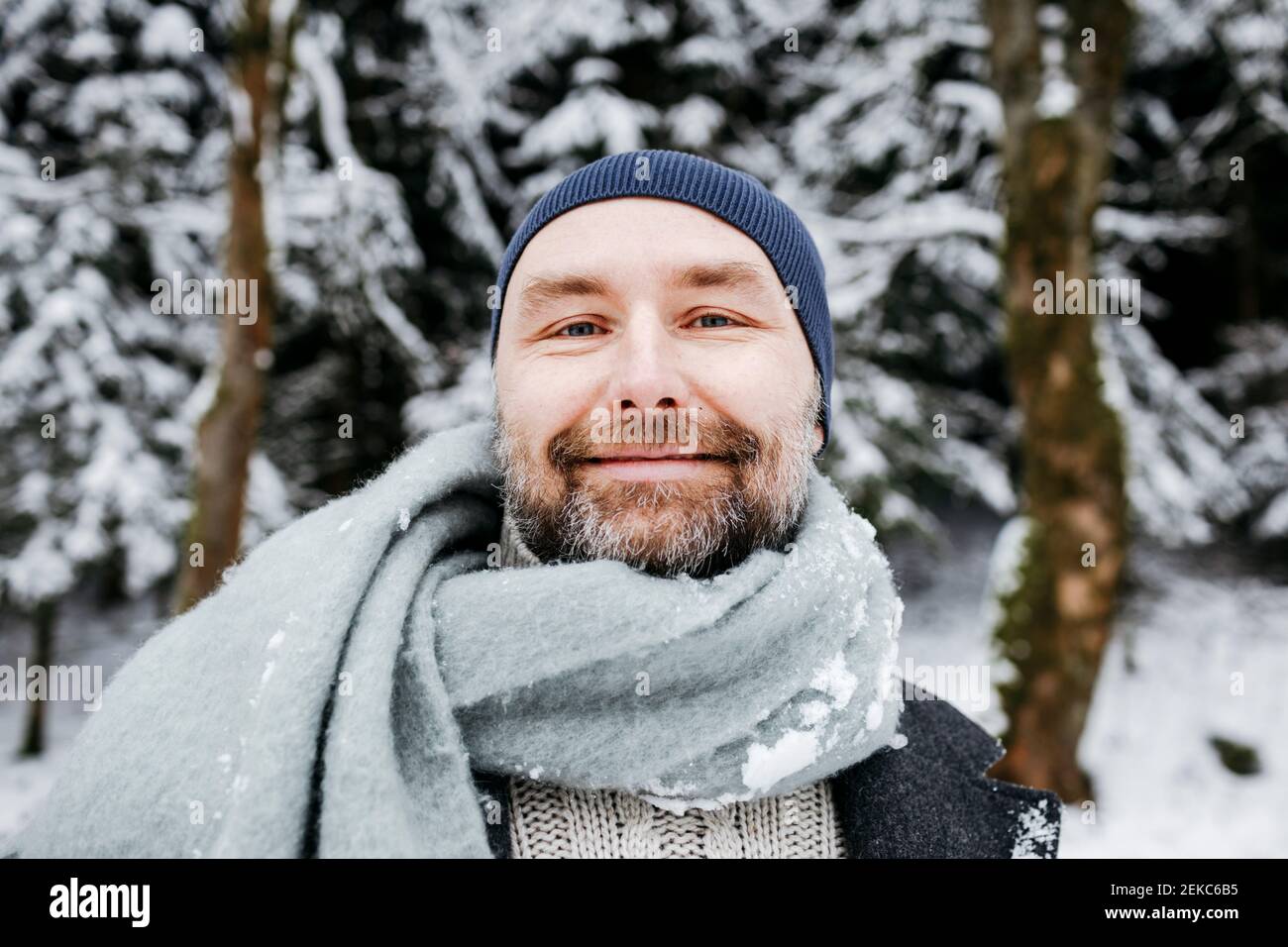 Lächelnder reifer Mann mit Schal auf Schnee während der Ferien Stockfoto