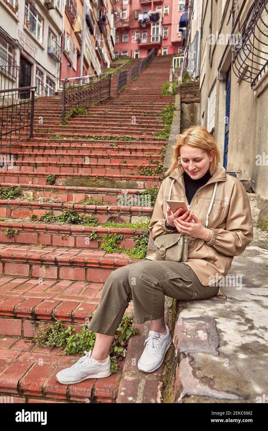 Lange rote Steintreppe im Wohngebiet von Istanbul in Europäische Seite und junge weiße Frau mit Sitz auf Beton Basis hält Smartphone whi Stockfoto