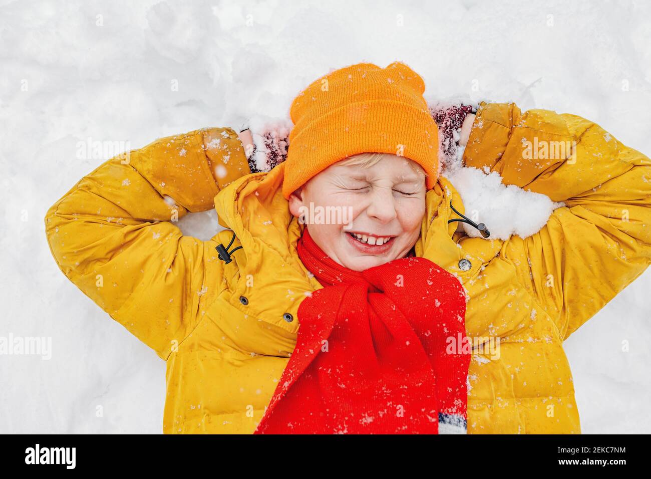 Glücklicher Junge mit Händen hinter dem Kopf auf Schnee liegen Stockfoto