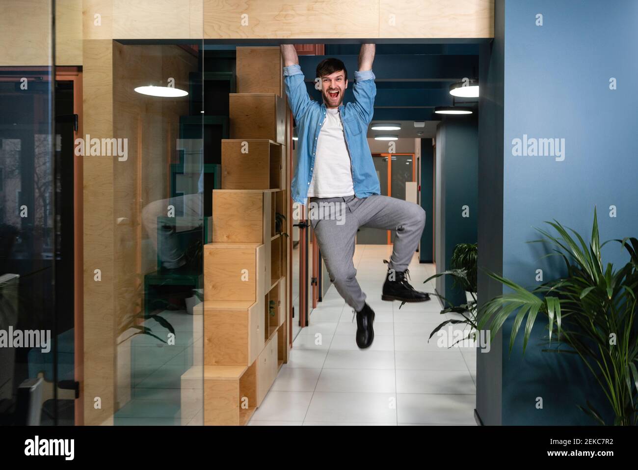 Fröhlicher Geschäftsmann, der an der Tür am Arbeitsplatz hängt Stockfoto