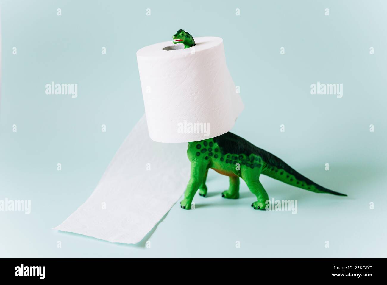 Diplodocus Dinosaurier Spielzeug mit einer Rolle Toilettenpapier herum Der Hals auf mintgrünem Hintergrund Stockfoto