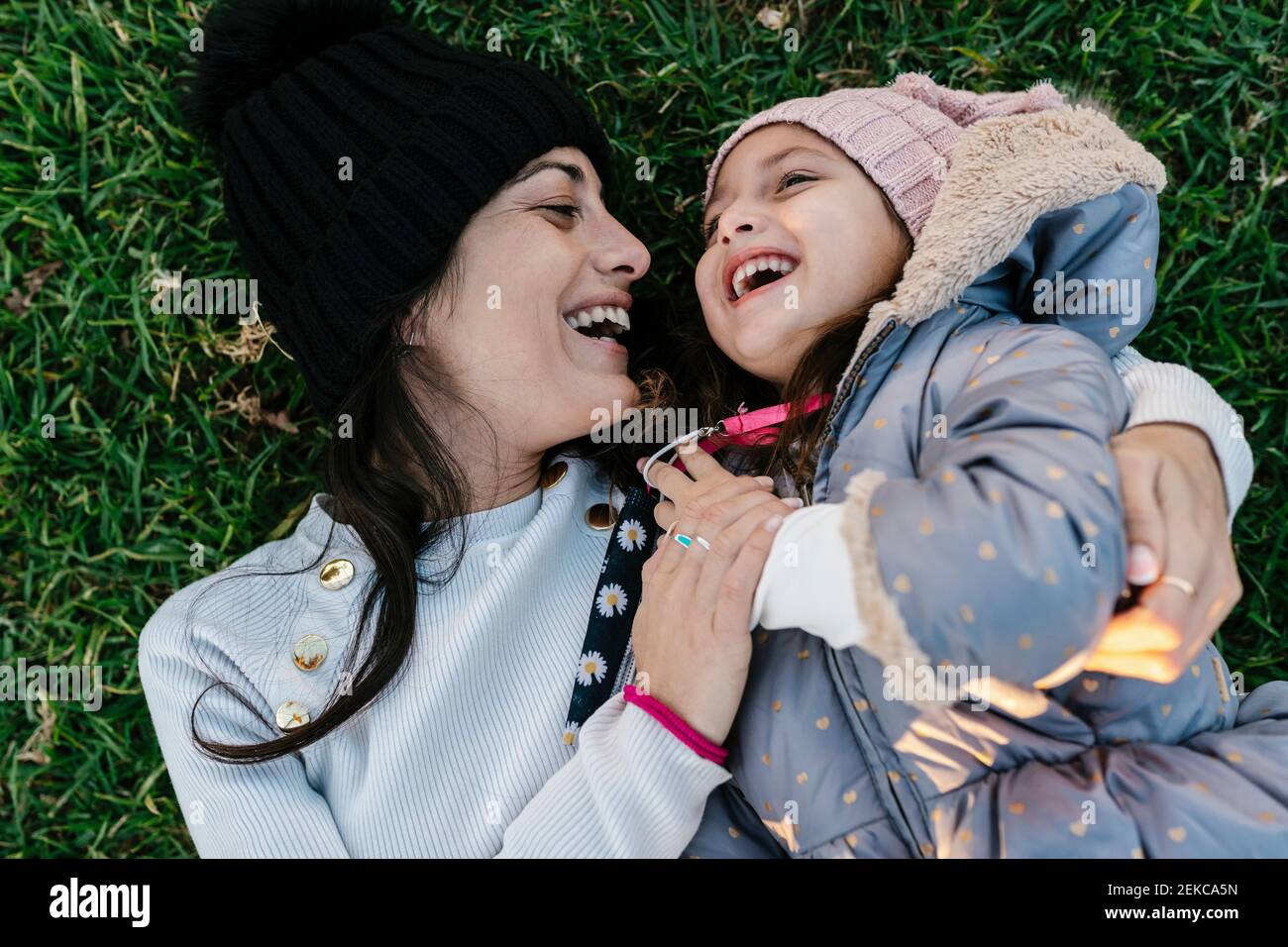 Lächelnde Mutter trägt Strickmütze und spielt mit Tochter, während sie liegt Auf Gras Stockfoto