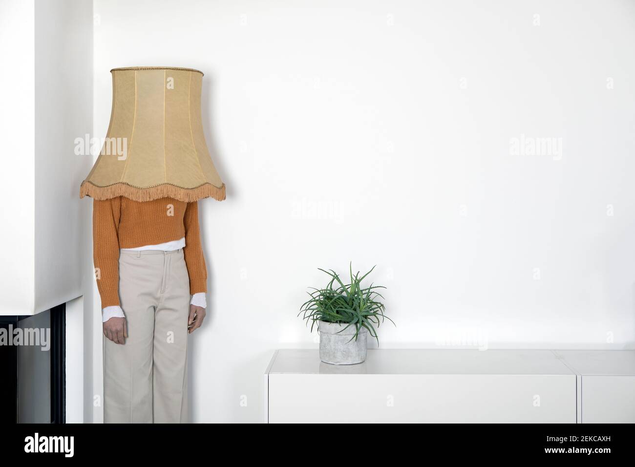 Reife Frau mit Lampenschirm auf dem Kopf, der gegen Weiß steht Wand  Stockfotografie - Alamy