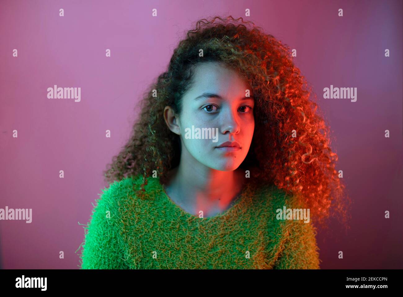 Rotes Licht auf schöne Frau mit lockigem Haar gegen Rosa Hintergrund Stockfoto