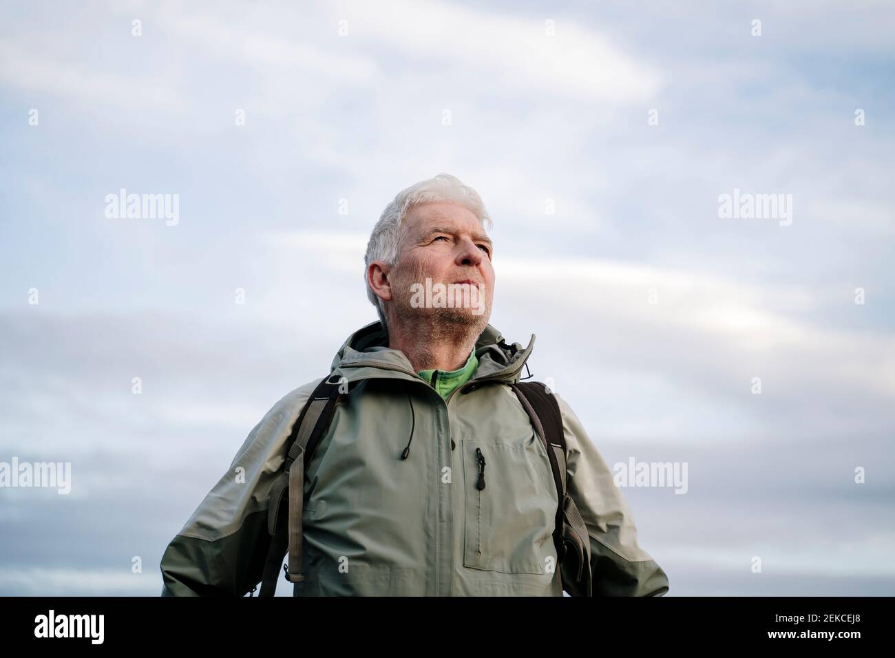 Älterer männlicher Wanderer schaut weg, während er gegen den bewölkten Himmel steht Am Wochenende Stockfoto