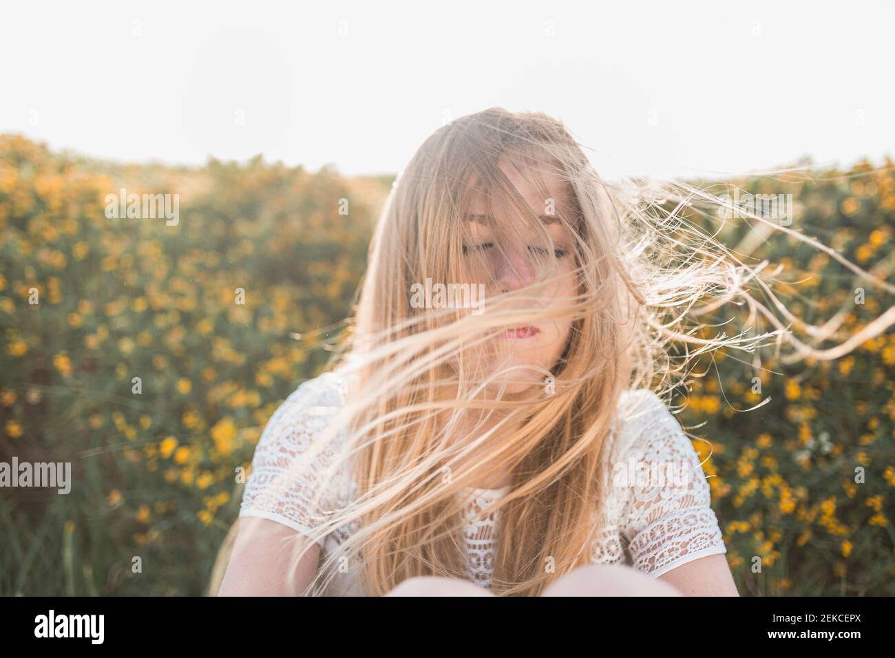 Wind weht Haare von jungen Frau, während sie auf dem landwirtschaftlichen Feld sitzt Stockfoto