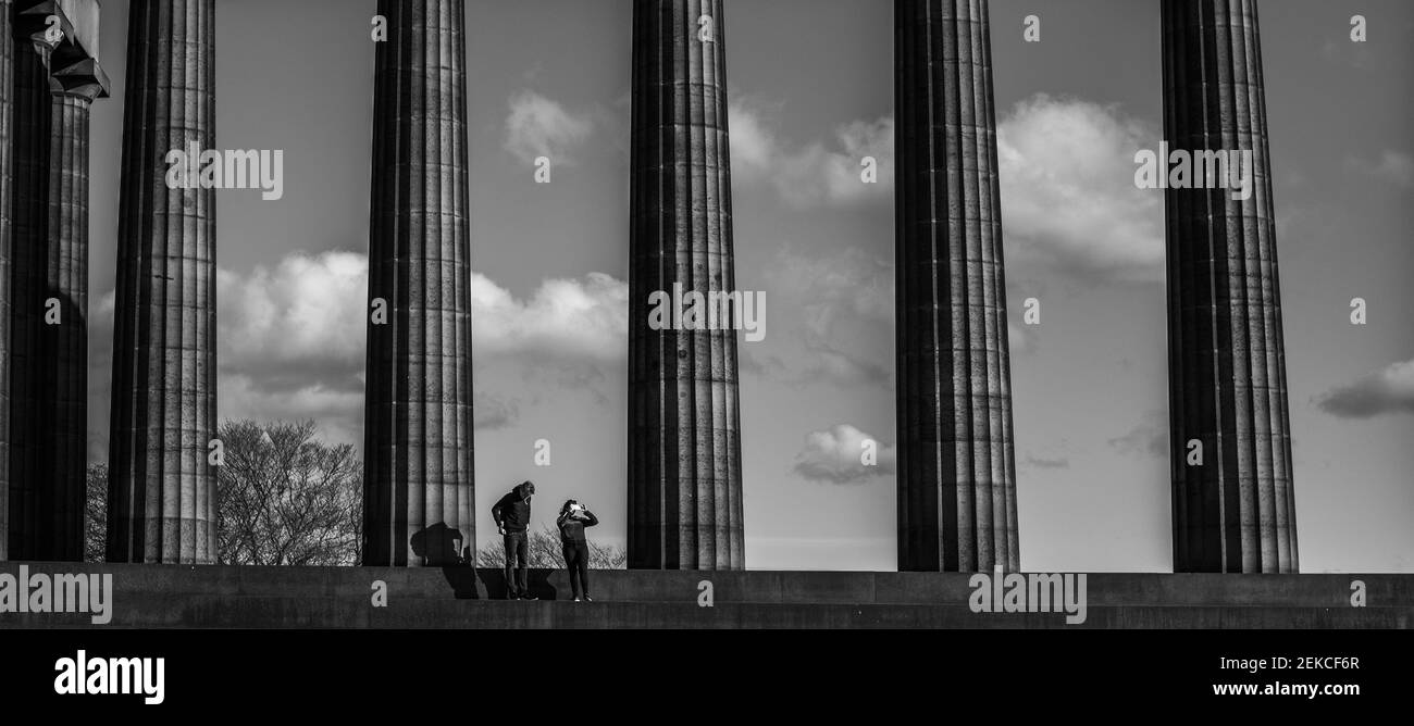 Einsames Paar auf den Stufen des Scottish National Monument auf Calton Hill, Edinburgh an einem sonnigen Tag während des Lockdown 2021. Aufgenommen in dramatischem Schwarz-Weiß Stockfoto