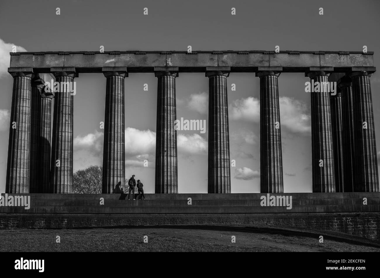 Einsames Paar auf den Stufen des Scottish National Monument auf Calton Hill, Edinburgh an einem sonnigen Tag während des Lockdown 2021. Aufgenommen in dramatischem Schwarz-Weiß Stockfoto