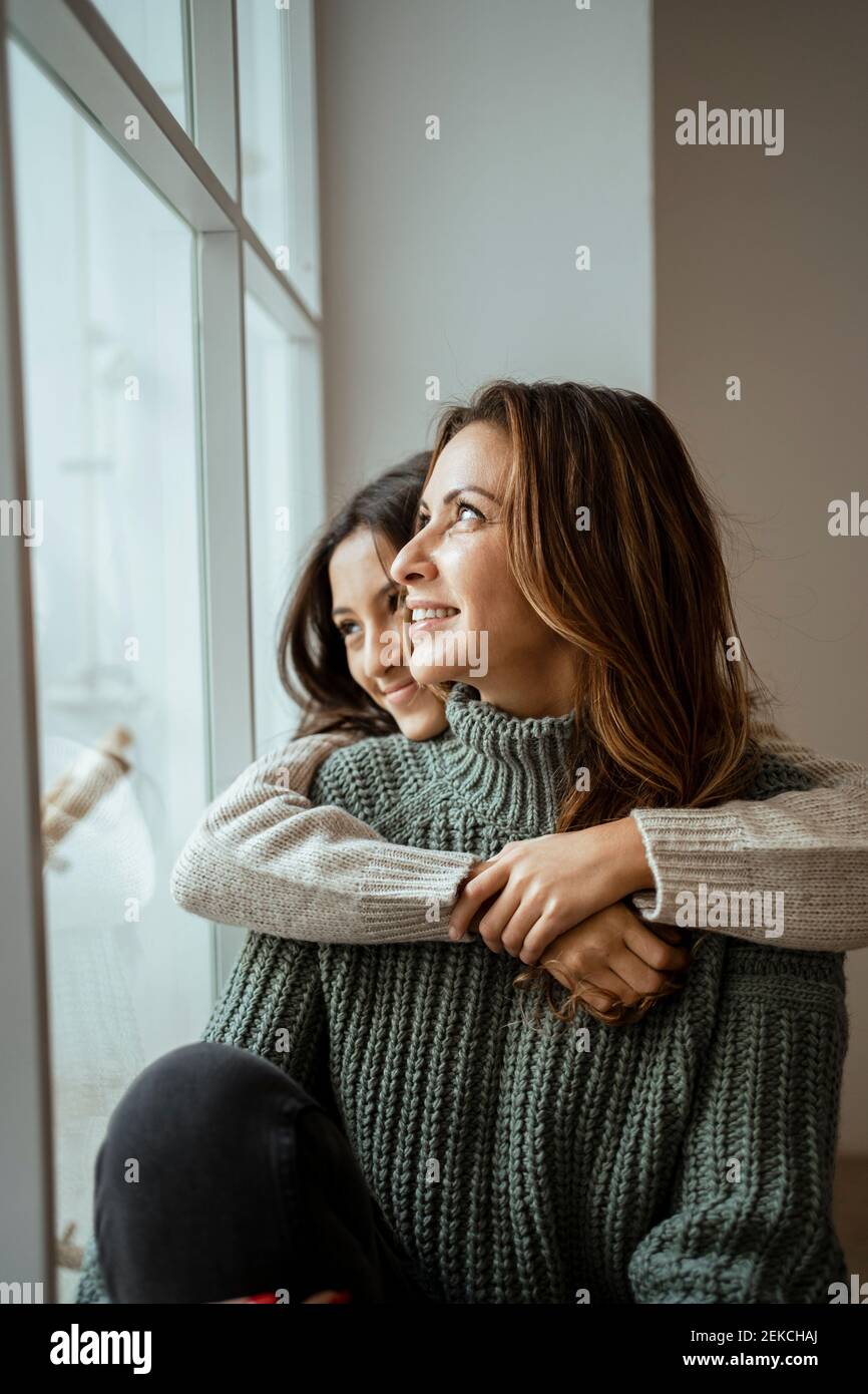 Glückliche Mutter und Tochter, die durch das Fenster schauen, während sie tagsüber träumen Gemeinsam zu Hause Stockfoto