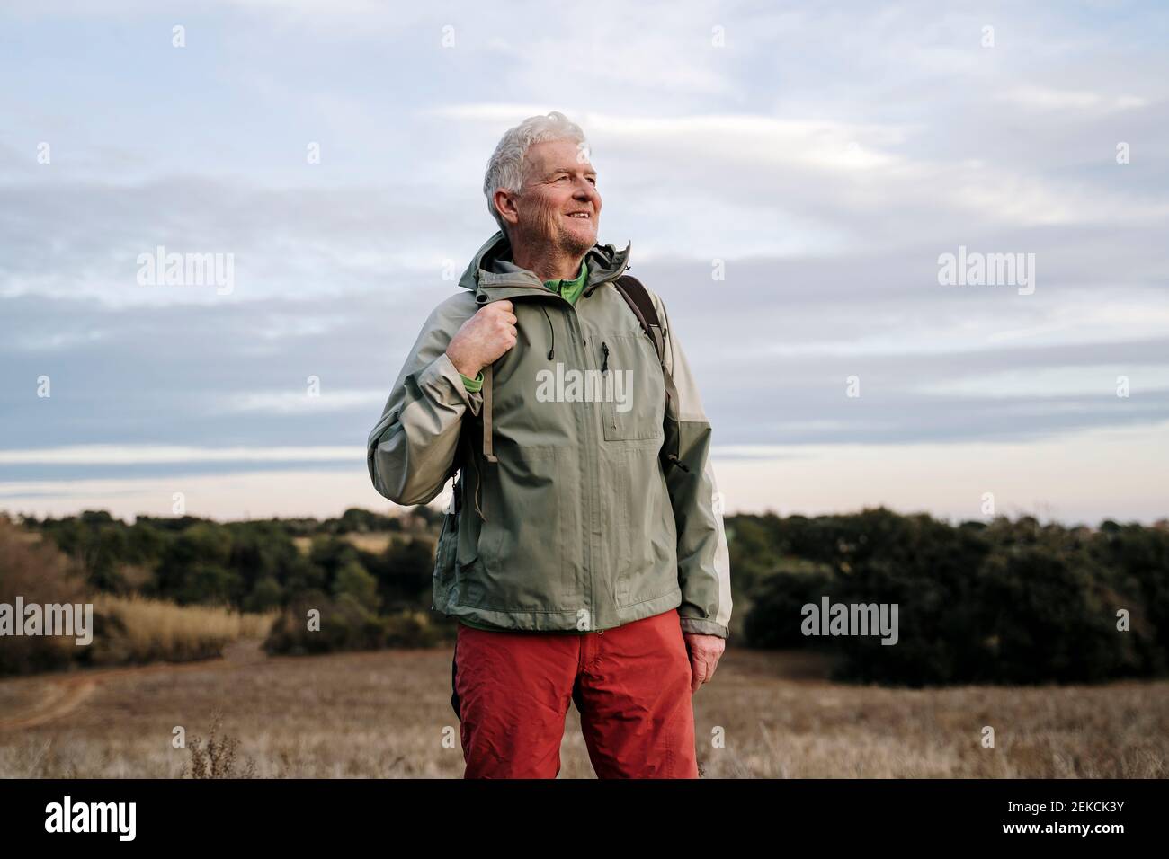 Lächelnder älterer männlicher Entdecker, der auf dem landwirtschaftlichen Feld gegen Wolken steht Himmel am Wochenende Stockfoto