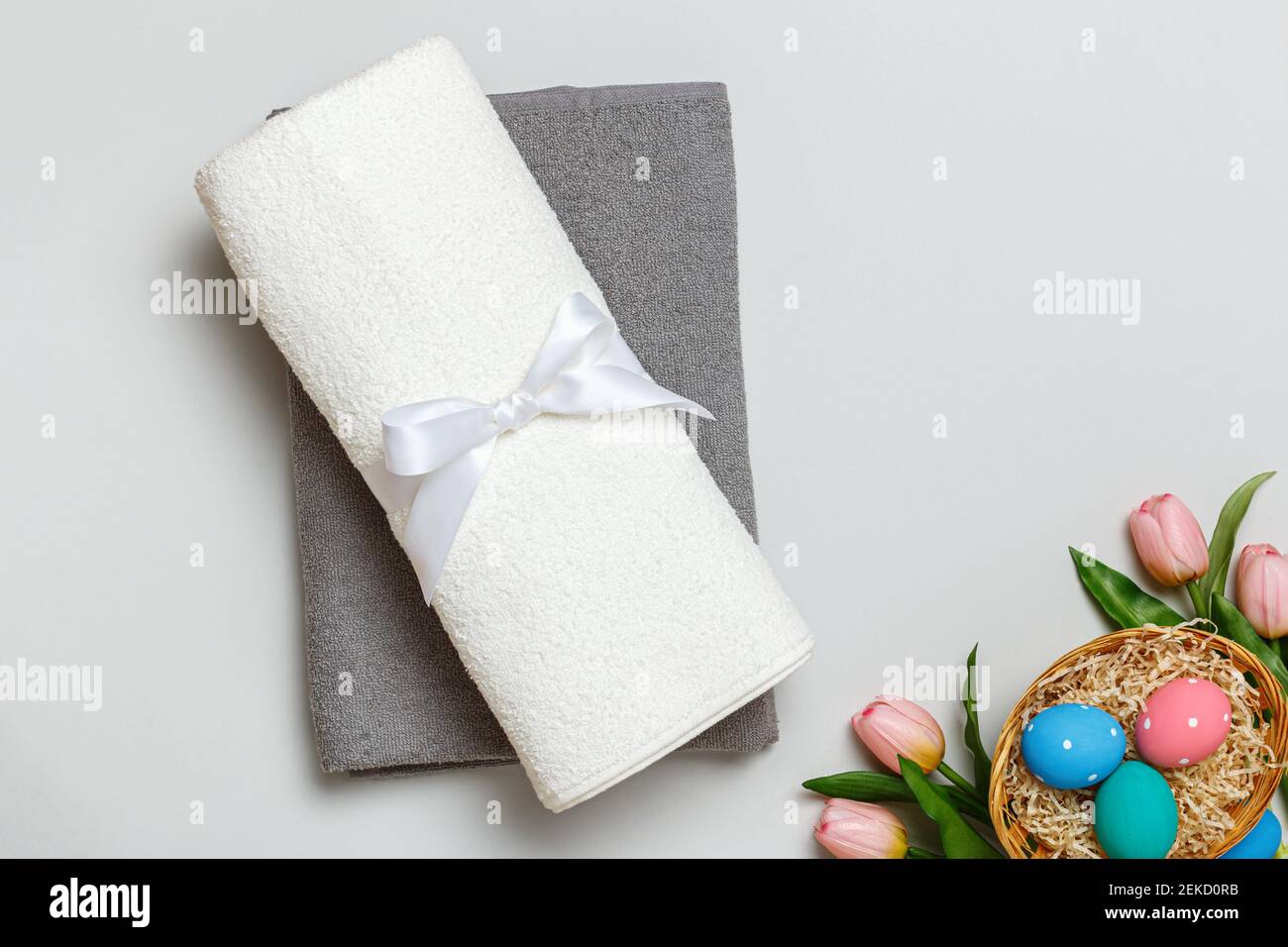 Draufsicht auf einen Stapel weißer und grauer Handtücher und einen Osterkorb voller Eier. Stockfoto