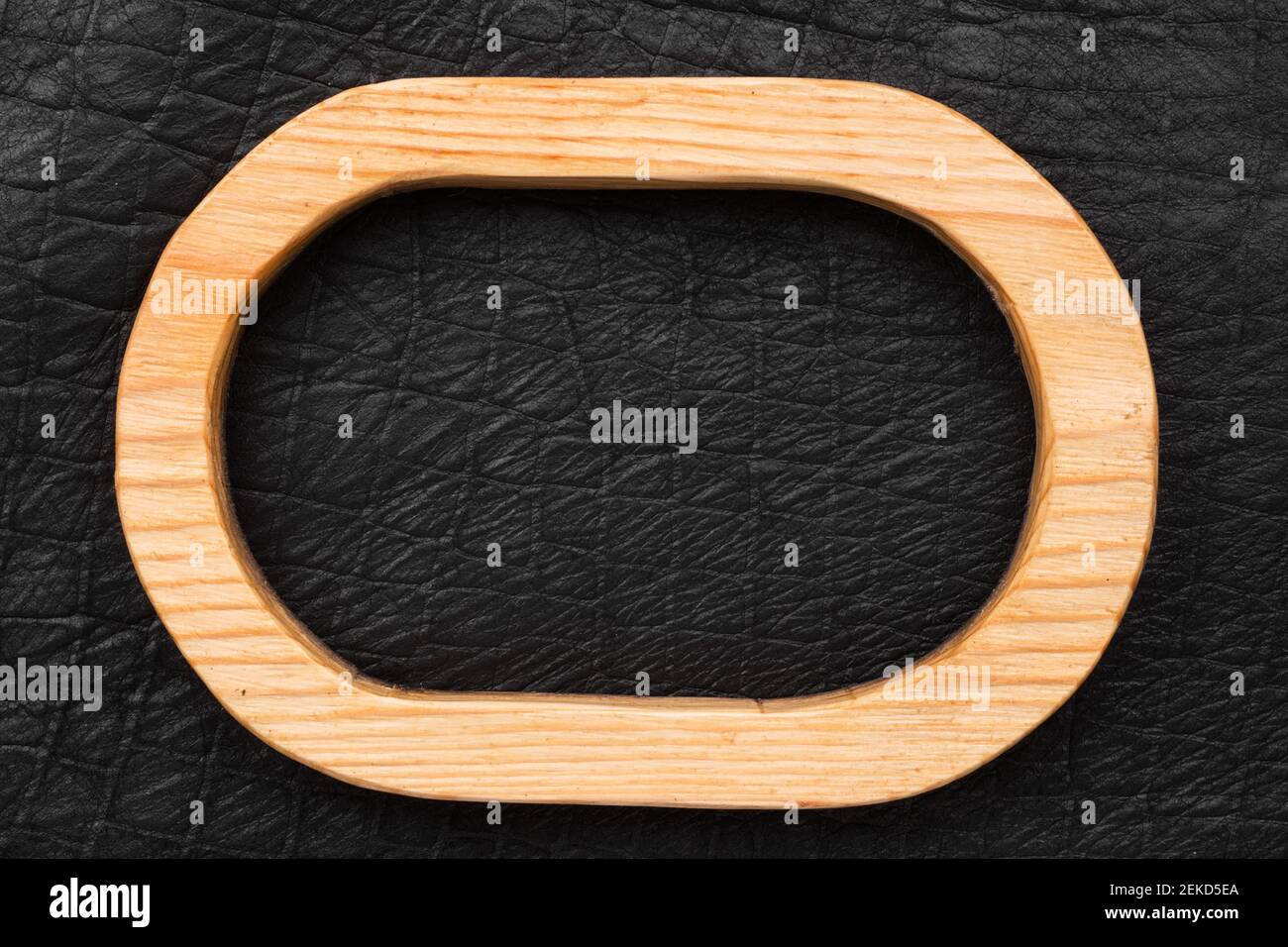 Ovaler Holzrahmen aus Holz liegt auf schwarzem Echtleder. Draufsicht. Schild, Tafel. Stockfoto