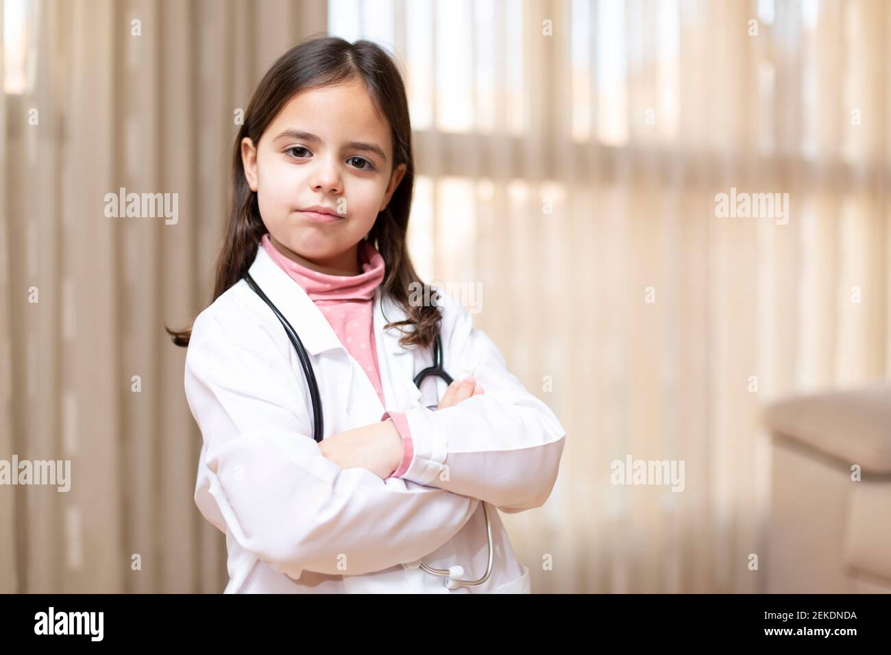 Porträt des kleinen Kindes in Arztuniform posiert mit gekreuzten Armen und verantwortungsvoller Haltung. Konzept von Medizin und Gesundheit. Leerzeichen für Text. Stockfoto