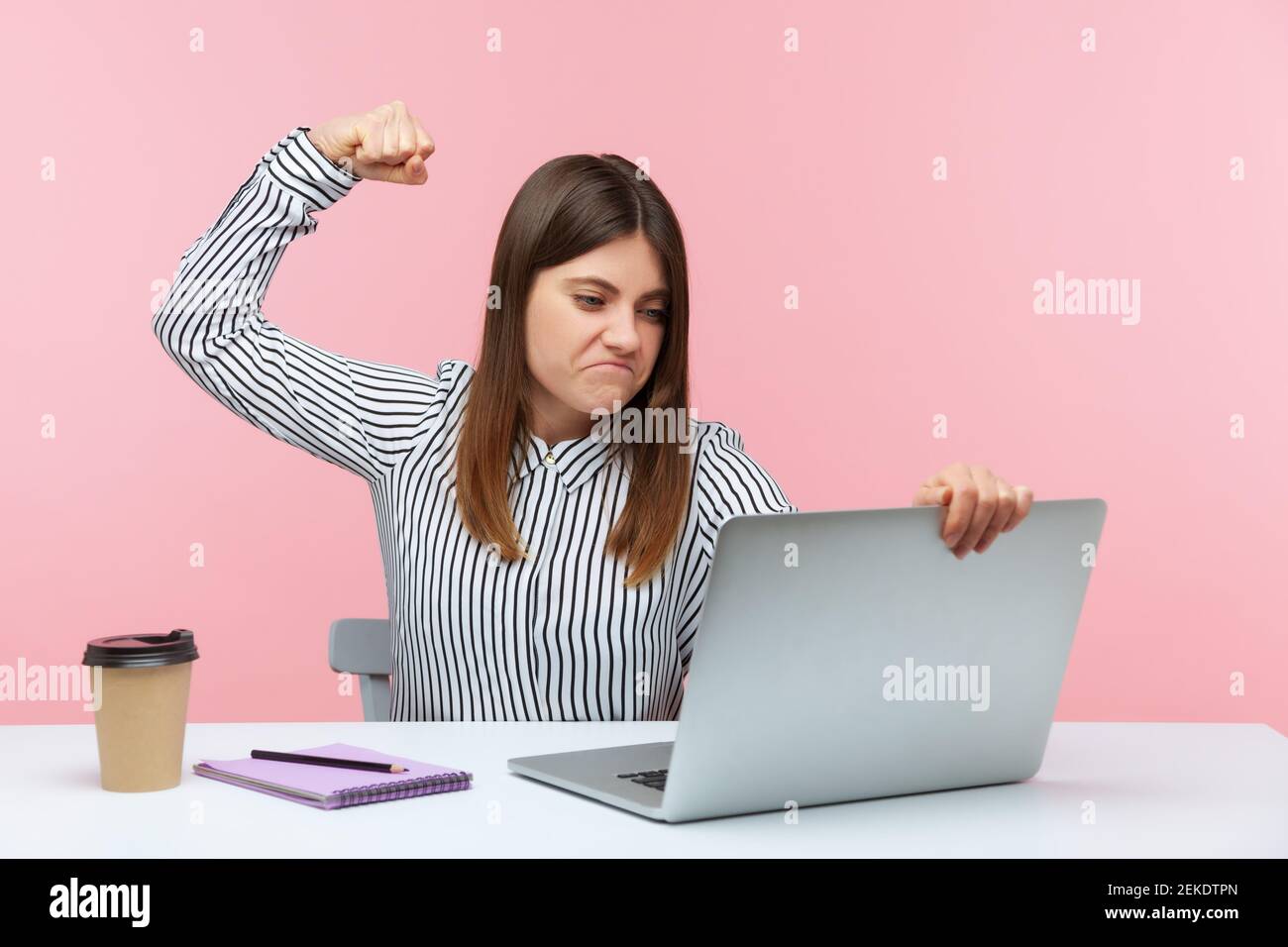 Aggressive depressive Brünette Frau Anheben der Faust bereit, um Laptop-Display am Arbeitsplatz sitzen treten, unglücklich unzufrieden mit Arbeitsergebnissen, Krise. Zoll Stockfoto