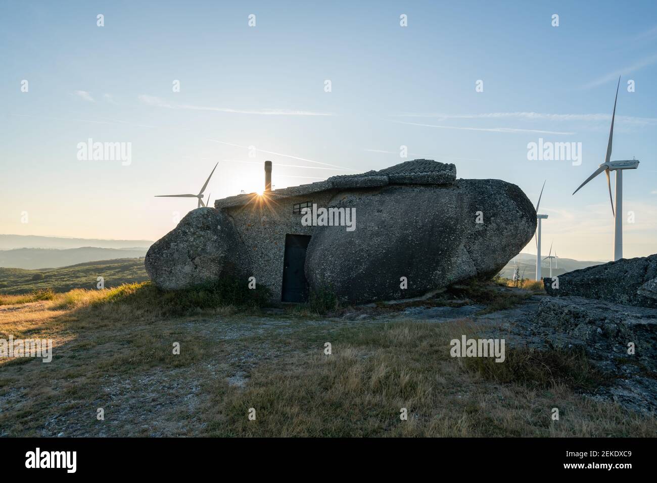 Schönes Stein Penedo Boulder House in Fafe, in Portugal mit eolischen Turbinen im Hintergrund Stockfoto