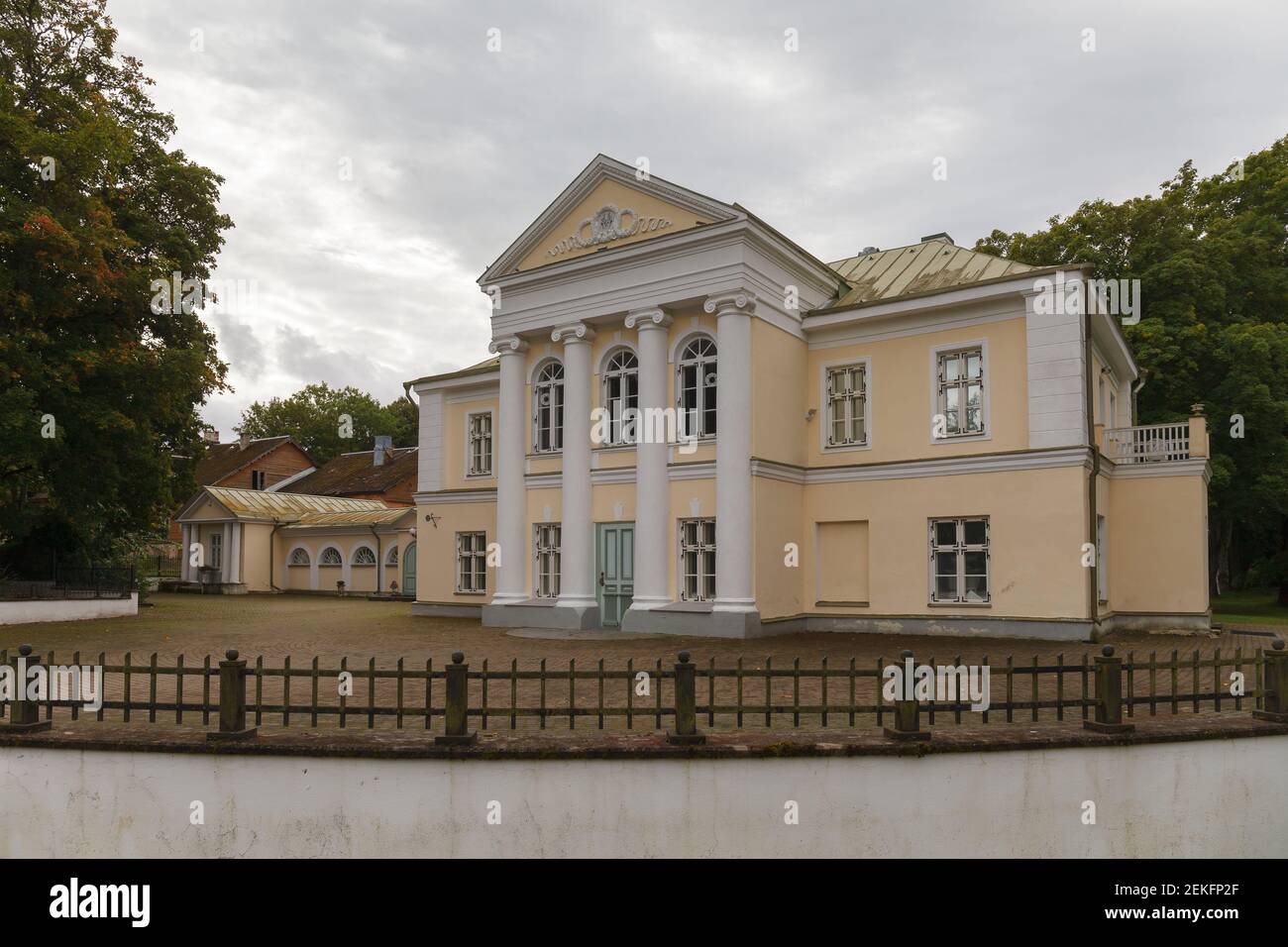 Vor dem Herrenhaus Kumna. Winziges mittelalterliches Gebäude, im neoklassizistischen Stil renoviert. Hellgelbe Wände, weiße griechische Säulen, Bogenfenster. Stockfoto