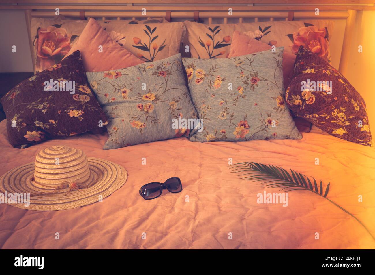 Eleganter Damenhut und Sonnenbrille auf einem stilvollen Bett. Warmes Licht. Das Konzept eines Sommermorgens, Urlaub, angenehme Entspannung, Vintage-Stil Stockfoto