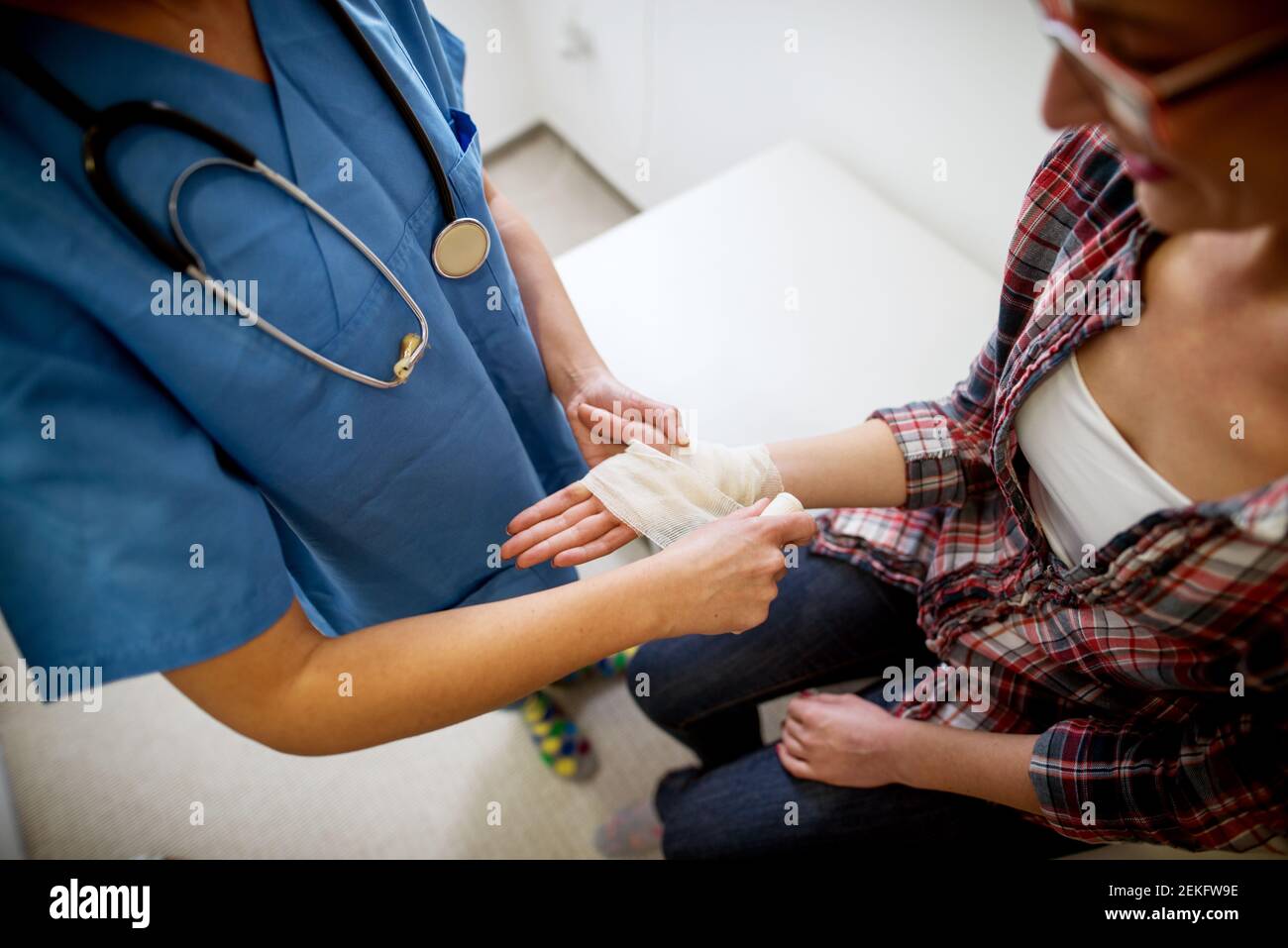 Nahaufnahme der Krankenschwester von oben, während sie der Patientin im Krankenhausbüro mit einem medizinischen Verband hilft. Stockfoto