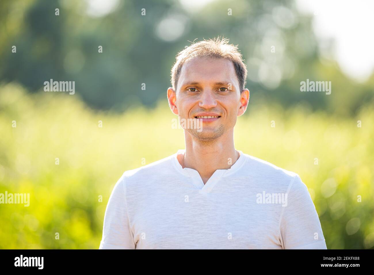 Bokeh grün weichen Hintergrund im Naturpark mit Nahaufnahme Porträt Von lächelndem jungen glücklichen Mann im Sommer in weißem Hemd Stockfoto