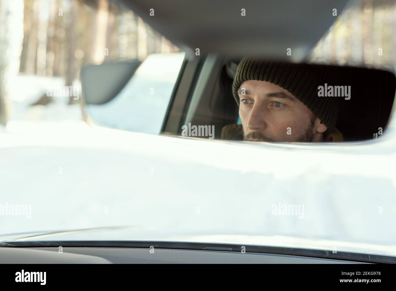 Spiegelung des Gesichts des jungen aktiven Mannes in Winterkleidung suchen Durch die Vorderscheibe des Autos während der Fahrt zum Landhaus Oder an einem anderen Ort Stockfoto