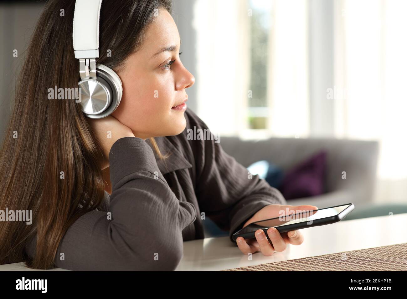 Nachdenkliche Frau, die kabellose Kopfhörer trägt und dabei nachdenkt, Musik zu hören Zu Hause Stockfoto