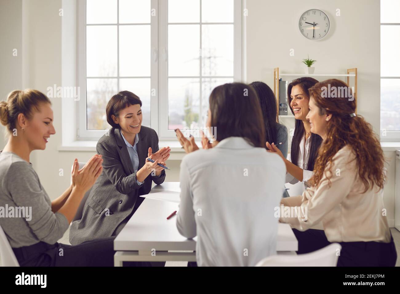 Team von glücklichen Geschäftsfrauen sitzen um Bürotisch und Einander applaudieren Stockfoto