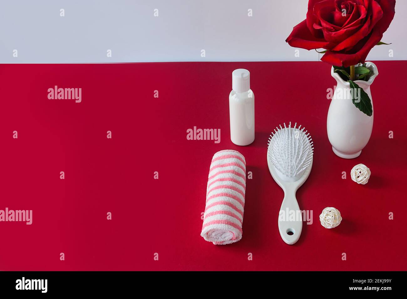 Haarpflegekonzept. Weiße Haarbürste, Shampoo und Handtuch auf rotem Samttisch mit Rosenblüte. Selektiver Fokus, Kopierbereich. Stockfoto