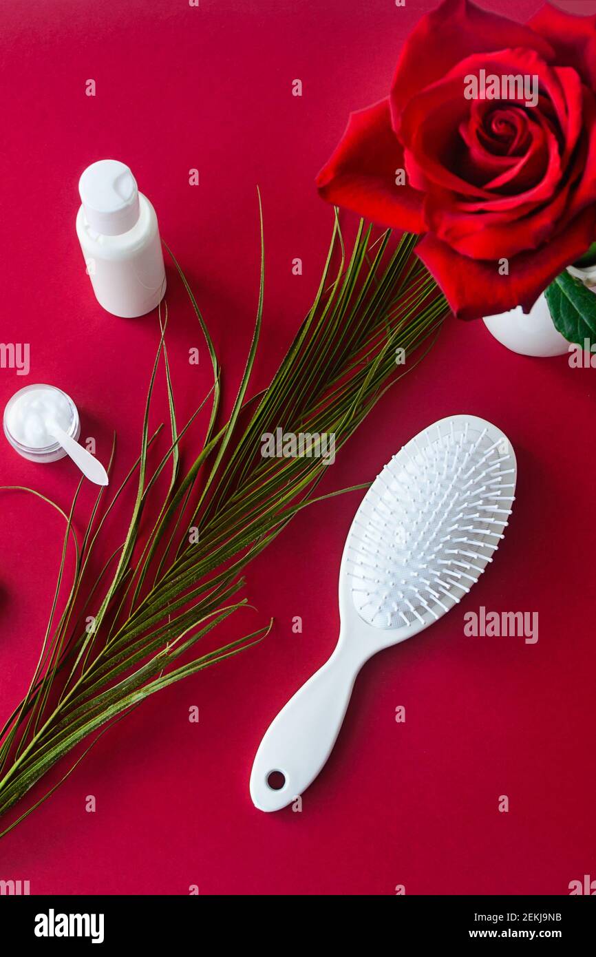 Weiße Haarbürste und Kosmetik auf rotem Samttisch mit Rosenblüte. Draufsicht, selektiver Fokus. Stockfoto