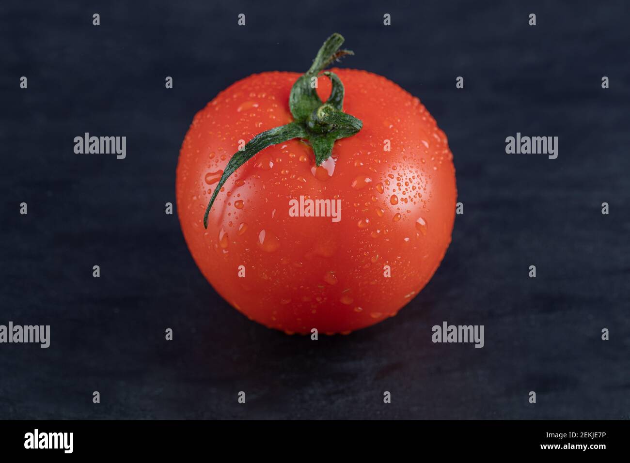 Eine frische Tomate mit Wassertröpfchen auf dunklem Hintergrund Stockfoto