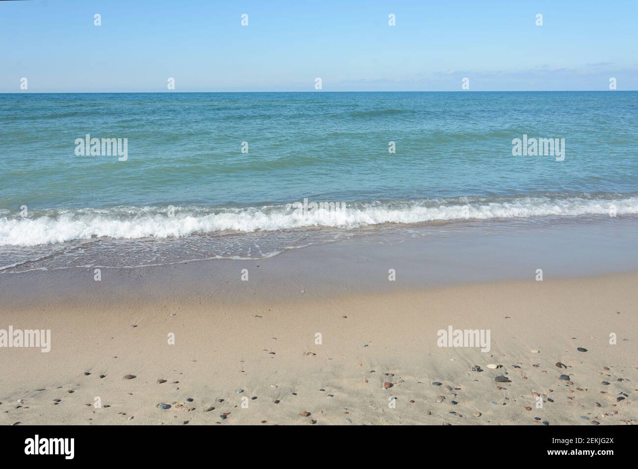 Sandige Küste mit kleinen Steinen. Surfen und Wellenreiten mit Nahaufnahme aus weißem Schaumstoff. Reisekonzept, Urlaub am Meer. Stockfoto